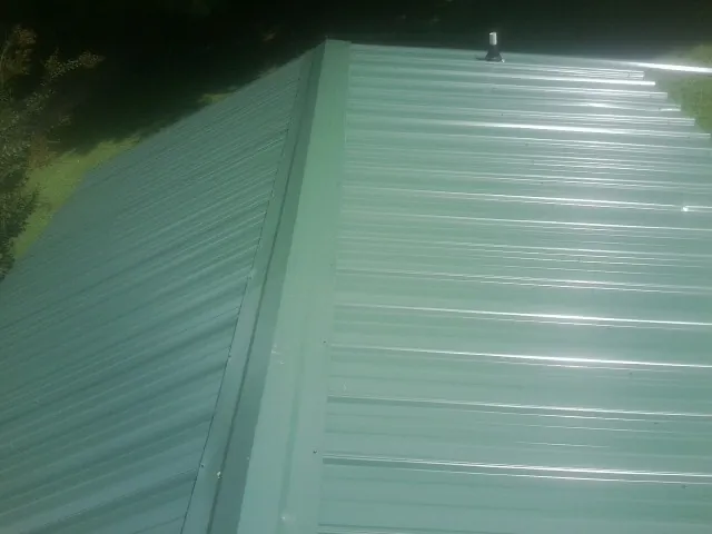 New green metal panels meeting at the ridge of a roof — Flat Roof Repair work by our crew in Gatlinburg