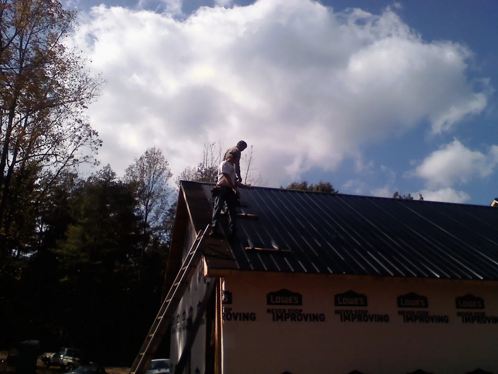 Roofer fastening dark metal panels high against a cloudy sky, from a Roof Inspection job in Gatlinburg