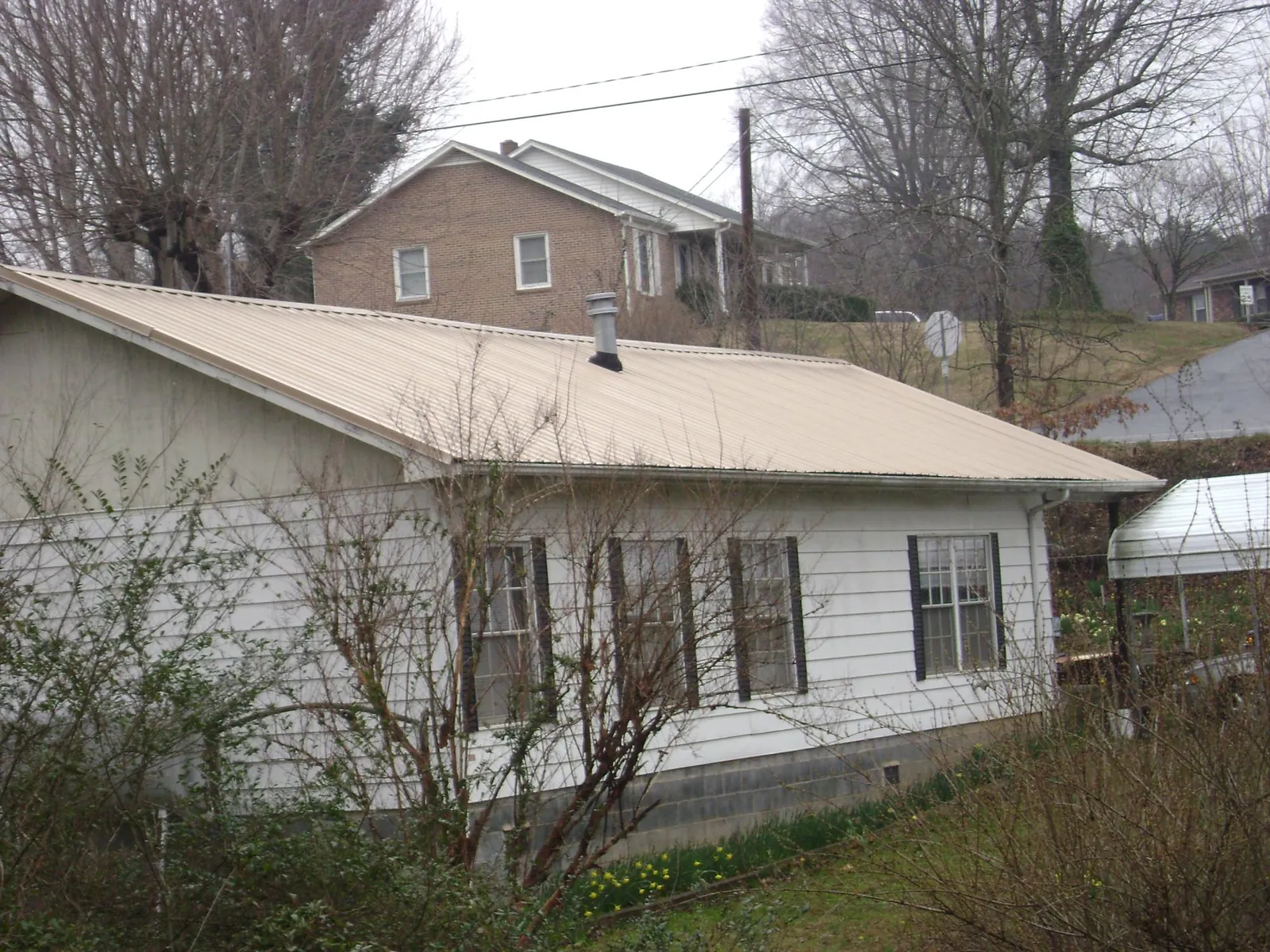 Tan metal roof on a white sided house set into a hillside — Commercial Roofing by Roofing Brothers in Gatlinburg